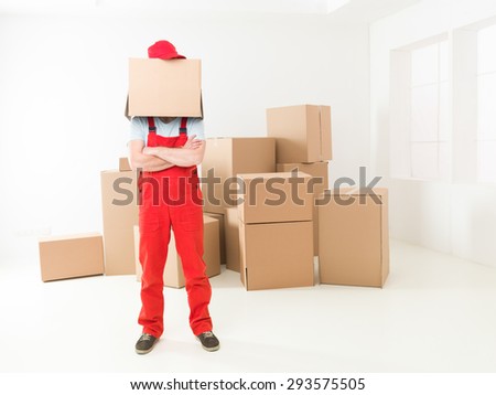 front view of deliveryman standing in new house with arms crossed against his chest, box covering his head