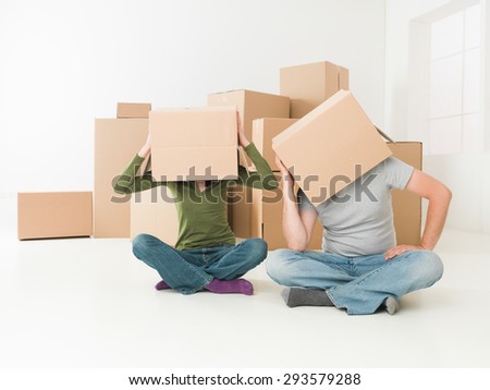 couple with boxes on their heads sitting on floor in their new house, feeling stressed