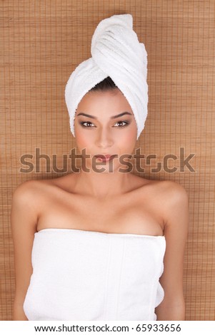 a portrait of a young woman at a day spa, layed on her back, on a mat, with her hair and body wrapped in white towels.