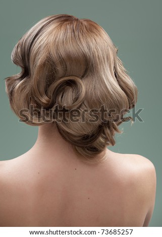 a head and shoulders image of a young woman, from the back. her hair is long and blonde and she is showing an interesting, wavy hairstyle.