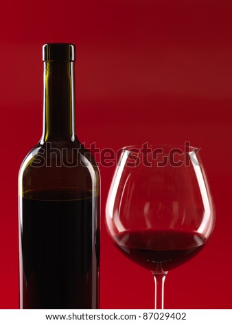 detail of bottle of wine and glass with red wine, on red background, copy space