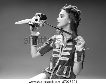 studio black and white fashion portrait of young woman in vintage outfit, posing with venetian mask