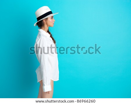 profile of young woman standing on blue background, with white hat and man\'s shirt, copy space