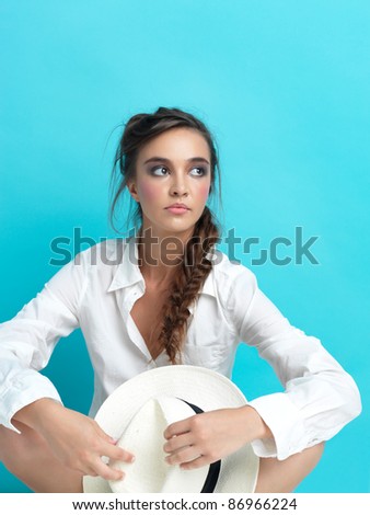 young woman sitting on blue background, with white hat and man\'s shirt, copy space