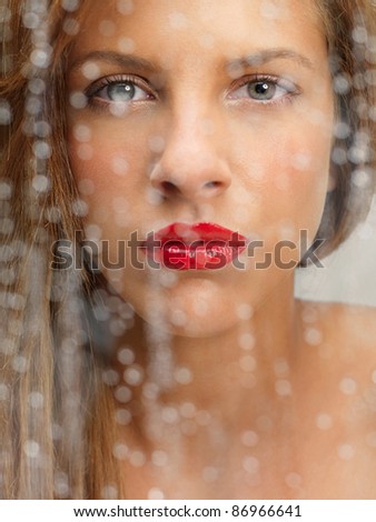 closeup beauty portrait of blonde woman looking at the camera from behind a wet window