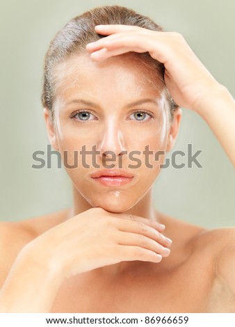 closeup beauty portrait of beautiful blonde woman with a facial mask on her skin, framing her face with her hands