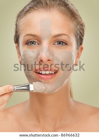 closeup beauty portrait of beautiful blonde woman applying a facial mud mask on her skin with a brush, smiling