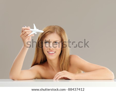 studio portrait of beautiful, young woman, playing with a small airplane model, smiling