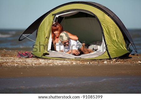 happy young sitting in a tent by the sea, talking, enjoying the summer vacation
