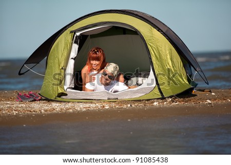 happy young sitting in a tent by the sea, talking, enjoying the summer vacation