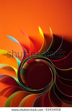 macro image of colorful curved sheets of paper shaped like a flower, on orange background