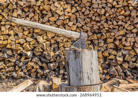 Axe stuck in a wooden log in front of the wood pile