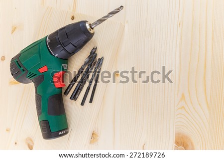 Electric drill and drill bits on a wooden board background horizontal