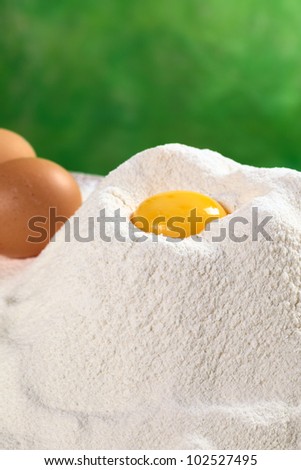 Flour with egg yolk in the middle with eggs in the back (Selective Focus, Focus on the upper front edge of the flour pile)