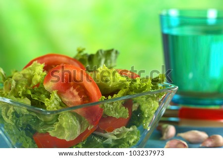 Fresh salad of lettuce and tomato with garlic and a glass of water in the back (Selective Focus, Focus on the tomato slice in the front)