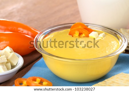 Peruvian Huancaina Sauce (spicy cheese sauce) made of cheese, crackers, aji (yellow chili) and milk in a glass bowl (Selective Focus, Focus on the front of the aji slices and the cheese on the sauce)