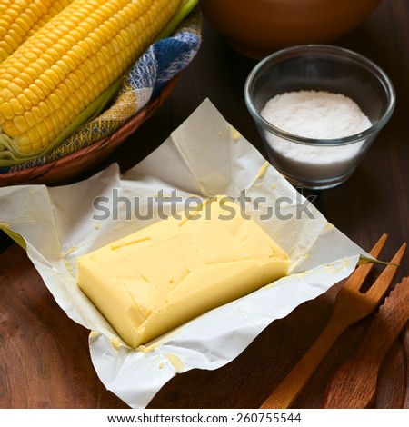 Piece of butter with salt and cooked sweetcorn photographed on wood with natural light (Selective Focus, Focus on the front of the butter)
