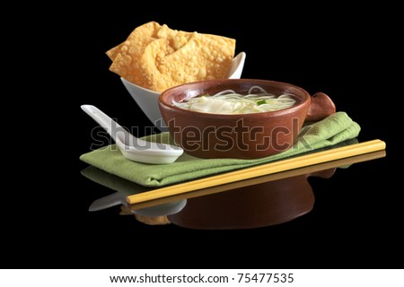 Chinese noodle soup with deep-fried wonton appetizer, ceramic spoon and chopsticks (Selective Focus, Focus on the front of the soup bowl)