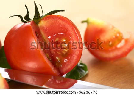 Globe tomato cut open on wooden board with a knife blade laying in front (Selective Focus, Focus on the seeds of the tomato)