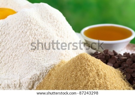 Granulated brown sugar with white flour, chocolate chips and honey in the back (Selective Focus, Focus on the top of the sugar pile)