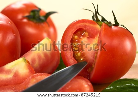 Globe tomato cut open on wooden board with a knife blade in front (Selective Focus, Focus on the seeds of the tomato)