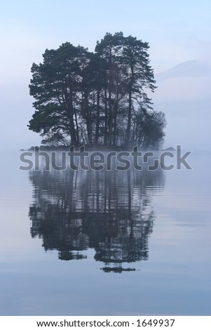 Small tree-covered island rises out of the mist on Loch Tay, Perthshire, Scotland