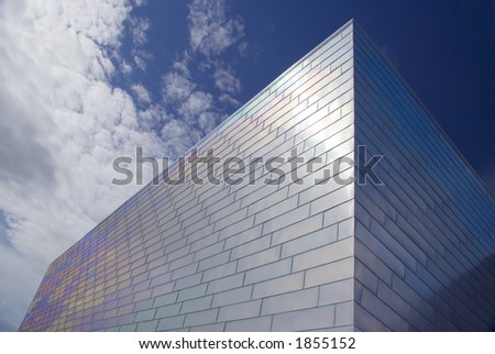 The face of a modern titanium-clad building against a blue sky