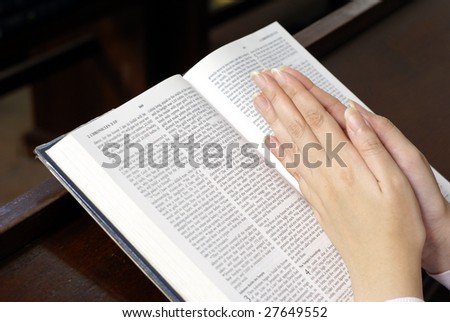 Hands praying on open bible