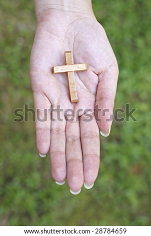 Female hand with wooden cross in palm and green background