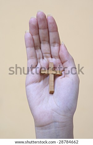 Female hand with wooden cross in palm and  light brown background