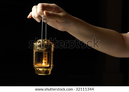Female hand holding metal candle lantern with lit flame