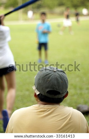 Family playing softball together, focus on father wearing cap