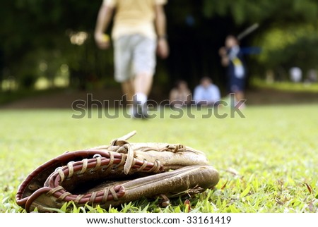 People playing softball outdoors with focus on catcher's glove on grass