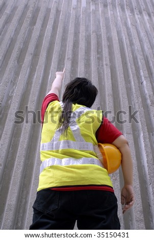 Asian female contractor pointing upwards with half finished wall