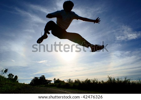 Silhouette of person jumping over sun with blue sky and clouds