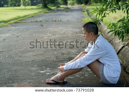Sad bald asian woman seated on ground outdoors