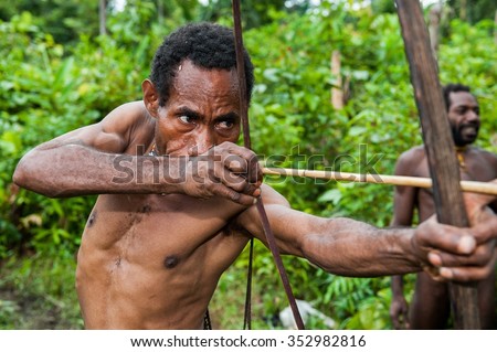 INDONESIA, NEW GUINEA, IRIAN JAYA, ONNI VILLAGE - JUNE 27, 2012: The Papuan from a Korowai tribe aims for shoots an archer. Korowai kombai (Kolufo) with bow and arrows on the natural forest background