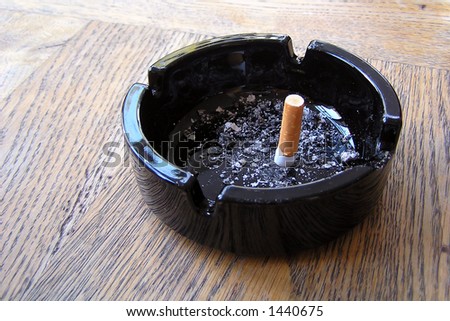 Finished cigarette in black ashtray with some ash.