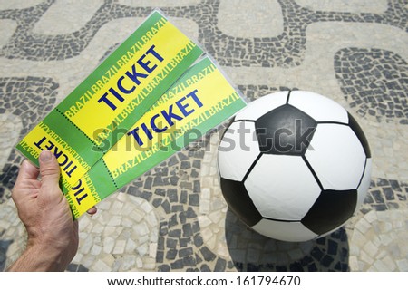 Hand holds two handmade tickets above football soccer ball in Rio de Janeiro