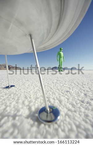 Little green man alien viistori standing under his flying saucer spacehip on strange planet surface