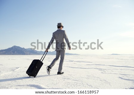 Traveling businessman walking with luggage across dramatic landscape