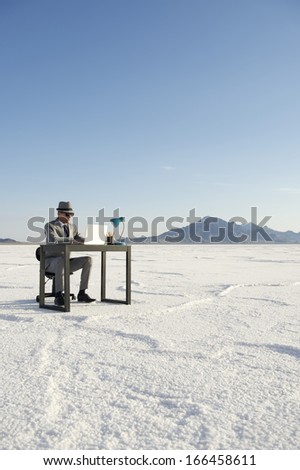 Businessman working on inspiration at desk outdoors on dramatic white desert landscape