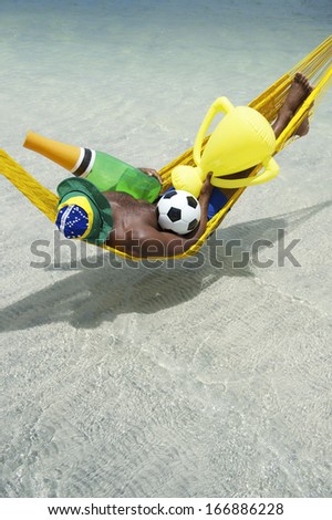 Brazilian dreaming of a football championship win with champagne and trophy and soccer ball in his hammock