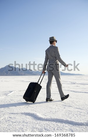 Traveling businessman walking with luggage across dramatic desert landscape