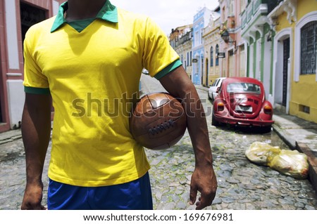 Brazilian soccer player standing on colonial Bahia street Pelourinho Salvador with vintage football