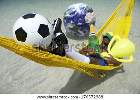 Champion Brazilian soccer player celebrating by relaxing in hammock with his football, champagne bottle, and trophy as the world floats by