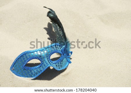 Glittery blue carnival mask with feathers on bright sand Brazilian beach