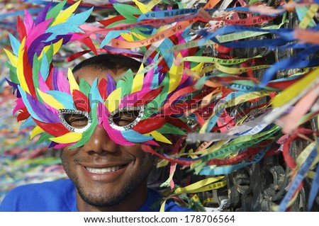 Rio Carnival scene features smiling Brazilian man in colorful mask with wish ribbons