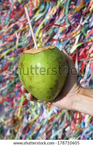 Brazilian hand holding coco verde gelado green drinking coconut at wall of wish ribbons in Salvador Bahia Brazil