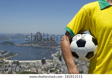 Brazilian soccer player holding football wearing shirt in Brazil colors at Rio de Janeiro skyline with Sugarloaf Mountain